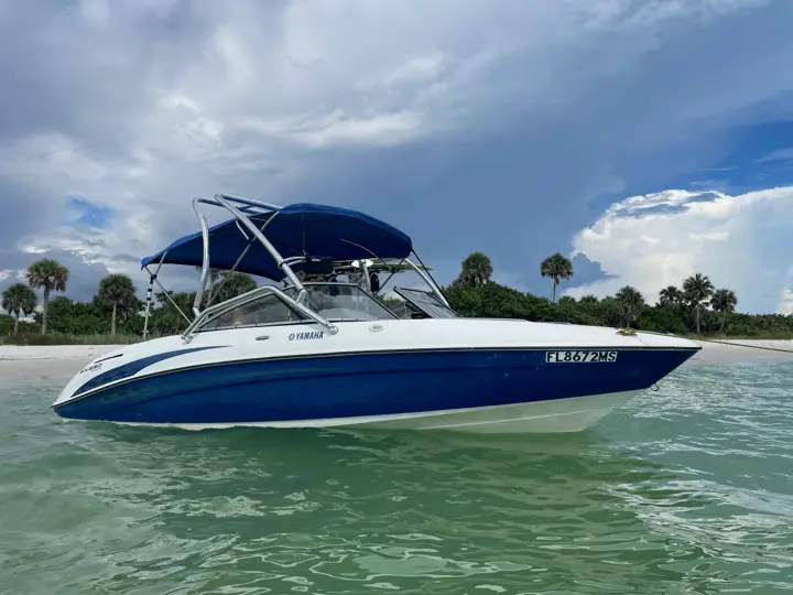 Yamaha SX230 jet boat rental in Naples, Florida, anchored in shallow Gulf water off a palm-lined beach with its wakeboard tower and blue Bimini top up